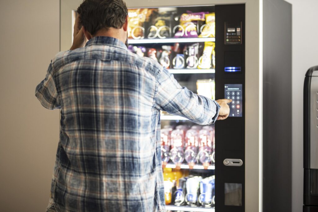 Hipster style man viewed from back buying snacks or drink from vending automatic